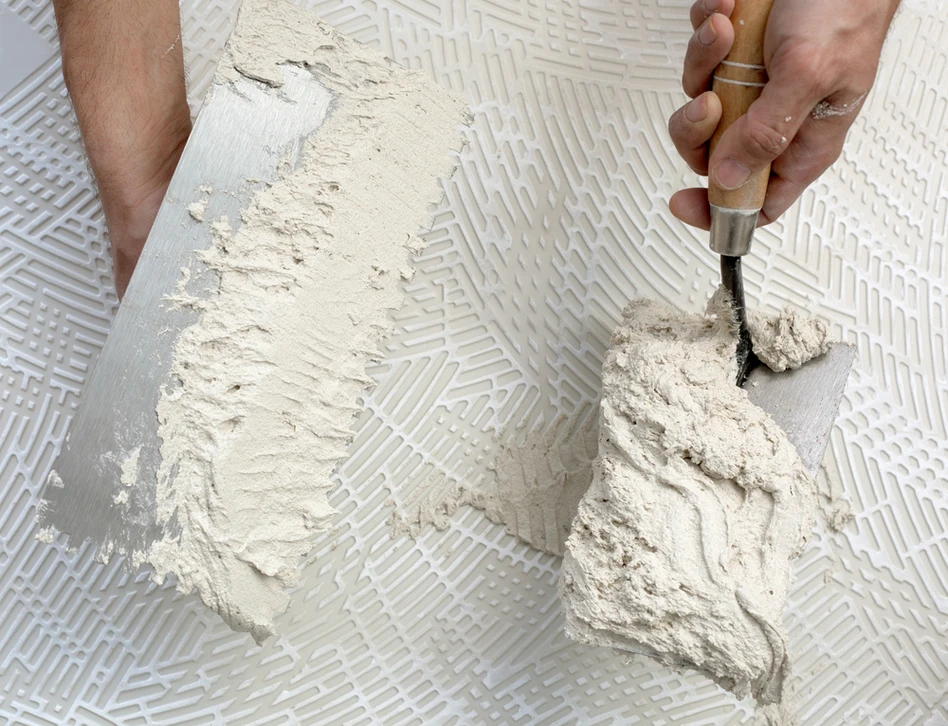 Artisan applique du mortier-colle sur carrelage mural avec une truelle crantée