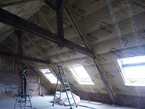Chantier de rénovation dans combles avec charpente bois apparente, murs en briques rouges