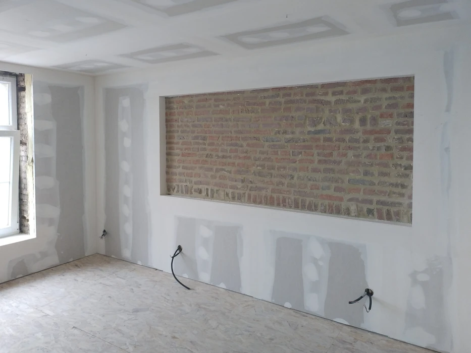 Chantier de rénovation intérieure en cours avec mur en briques apparentes encadré dans cloison placo