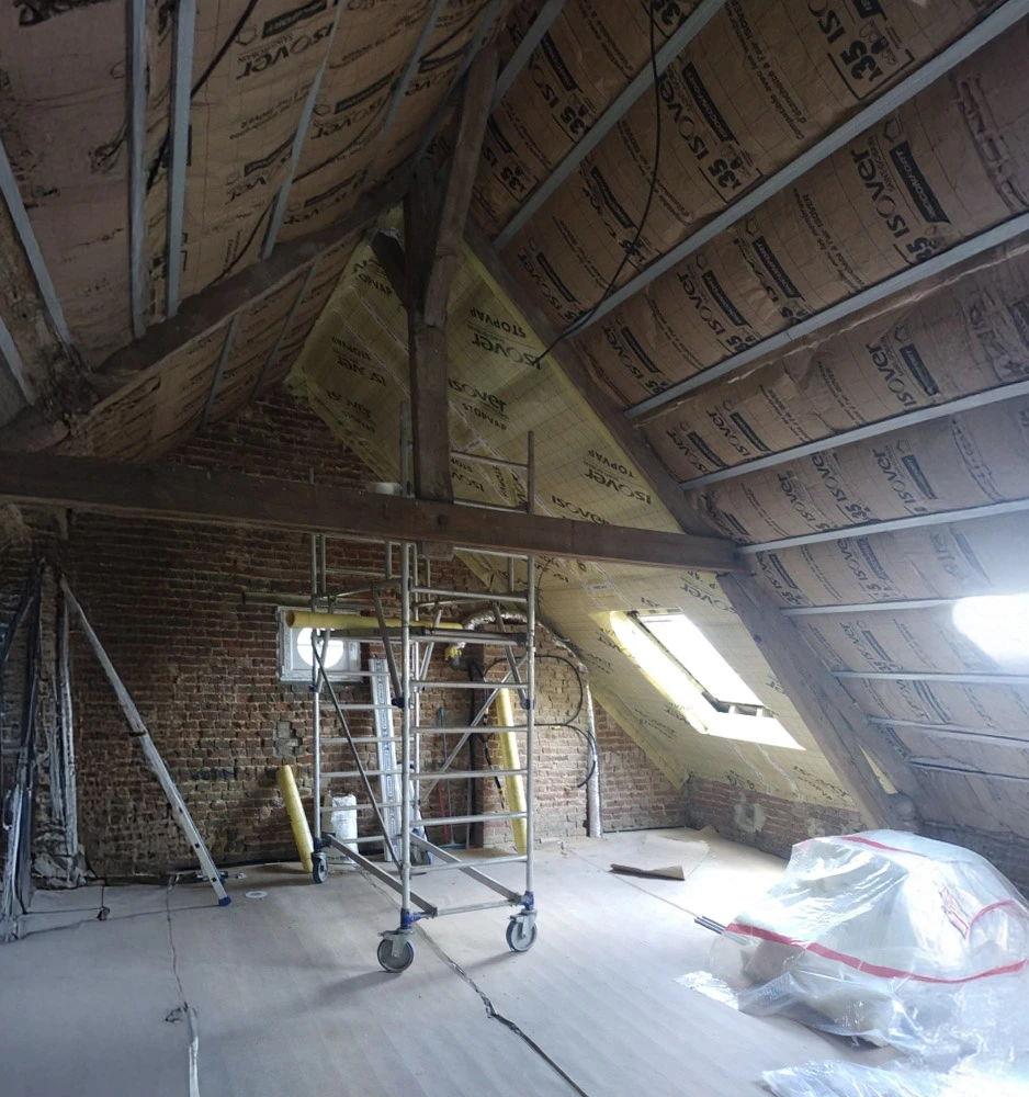 Chantier de rénovation dans combles en cours d'aménagement avec échafaudage mobile, murs en briques apparentes, isolation thermique sous toiture