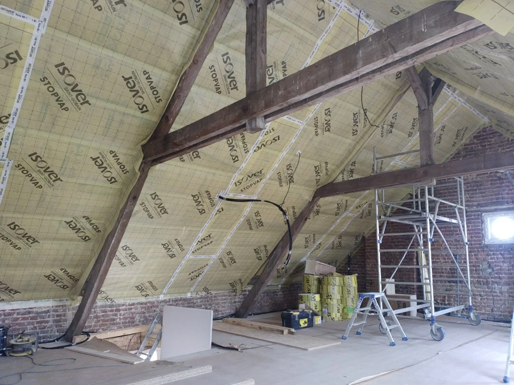 Salon moderne sous combles avec poutres apparentes blanches, canapé d'angle beige, coussins bleus, table basse noire