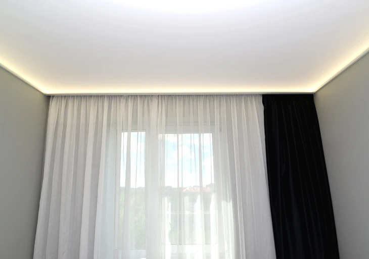 Main tenant un pinceau plat à manche bois appliquant une finition transparente sur lambris en bois naturel